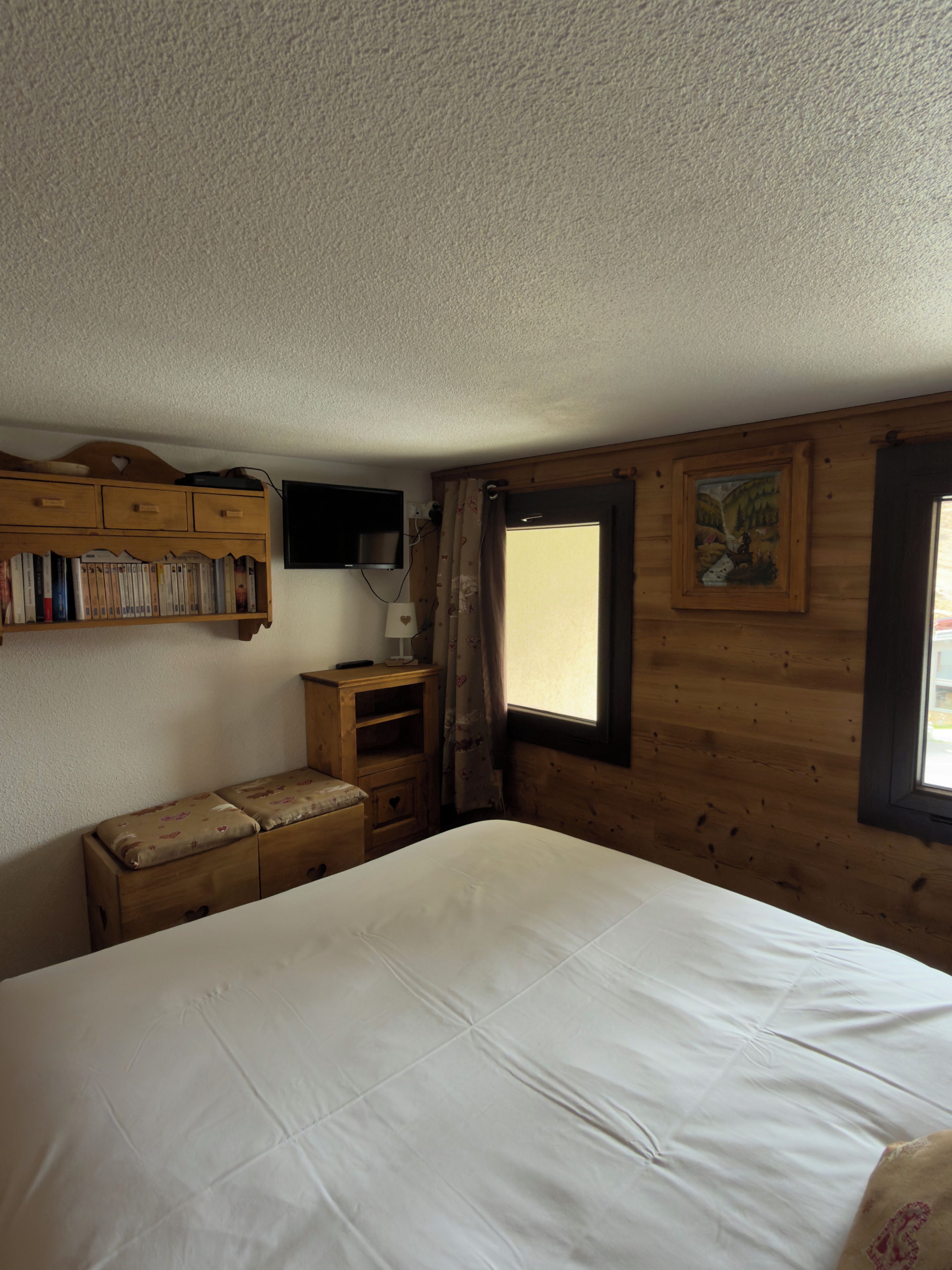 A bedroom with a bed, wooden dresser, and a television mounted on the wall.