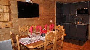 A wooden interior with a dining table set for four, a kitchen with dark cabinets, and a mounted flat-screen TV. - Apartment/ flat - VAL THORENS (Les Belleville)