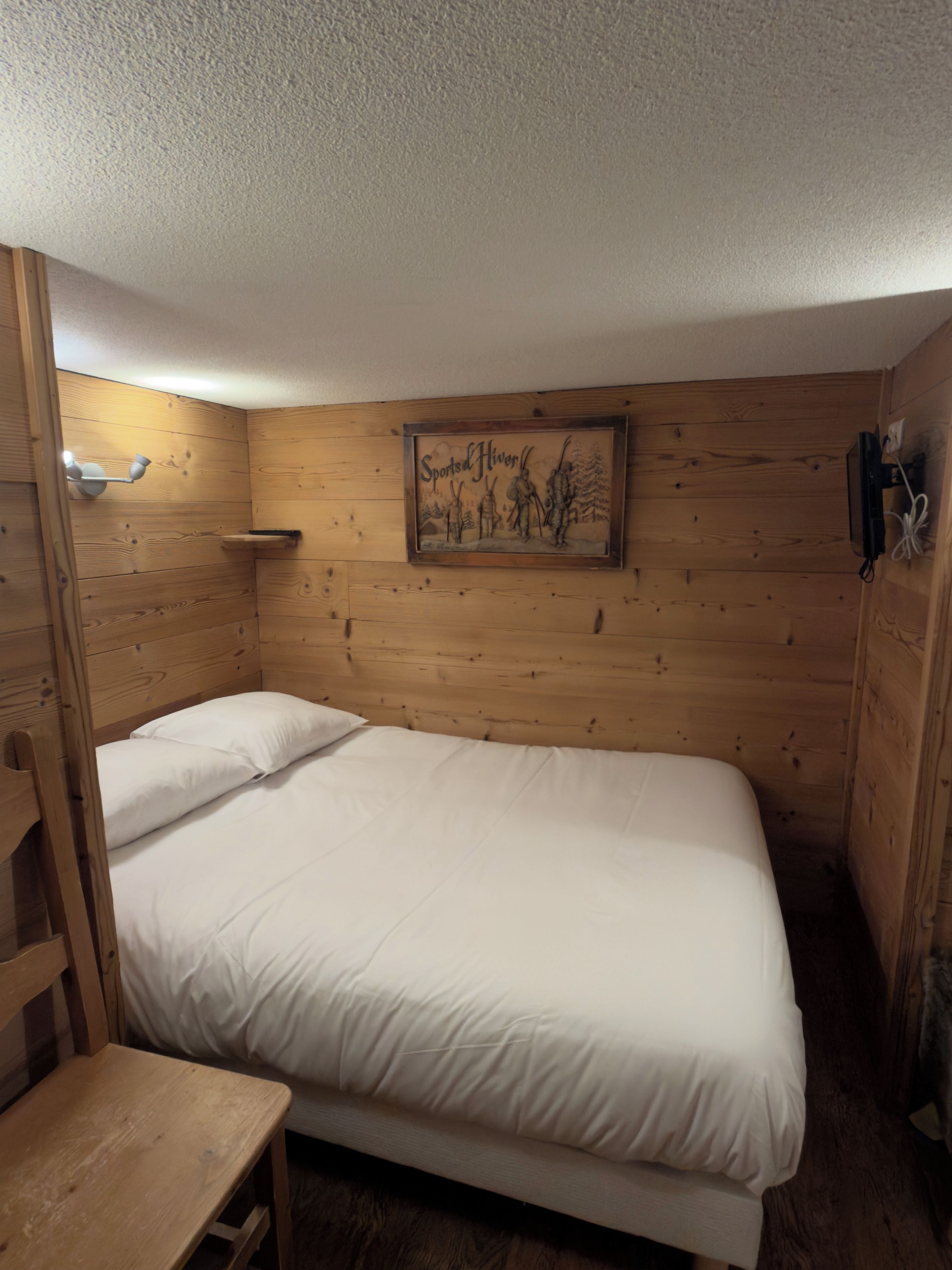 A single bed with white bedding in a wooden room with a wall-mounted picture frame.