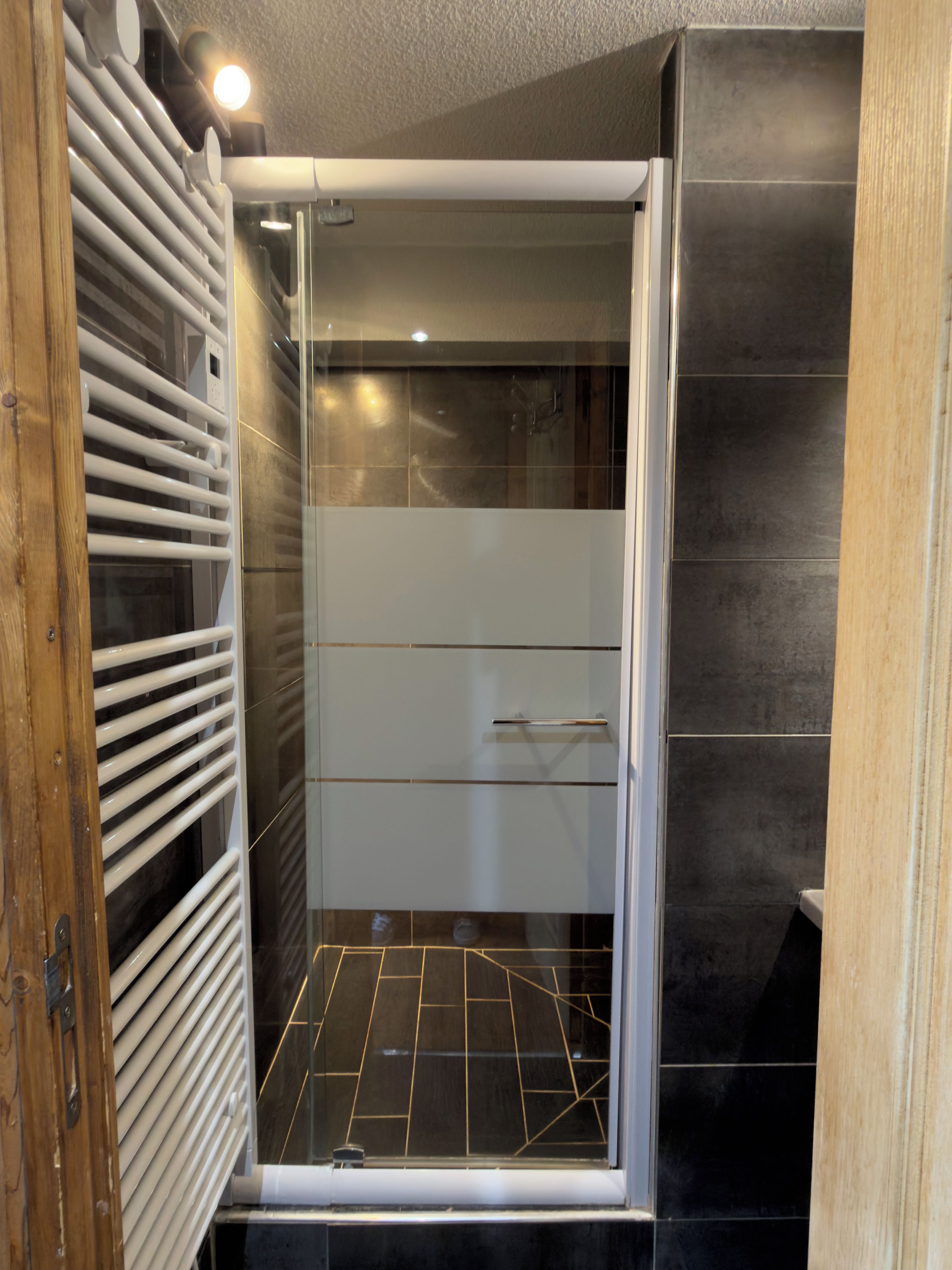 A shower with a glass door, a white towel rack, and a tiled floor.