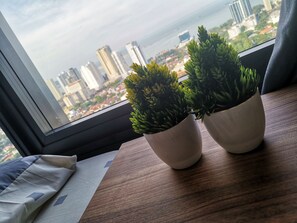 A window with a view of tall buildings and two potted plants on a wooden table.
