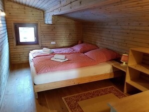 A wooden cabin bedroom with a bed, a window, and a small table.