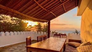 A wooden table and chairs under a thatched roof, with a view of the sea and a white fence. - Villa with pool, stunning sea views, with own chef and staff on request (Msambweni)