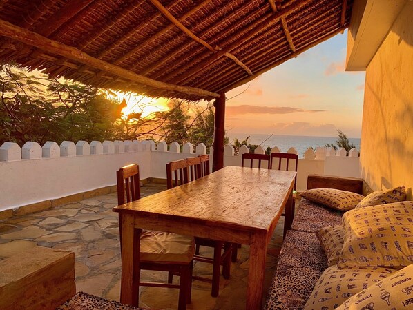A wooden table and chairs under a thatched roof, with a view of the sea and a white fence. - Villa with pool, stunning sea views, with own chef and staff on request (Msambweni)