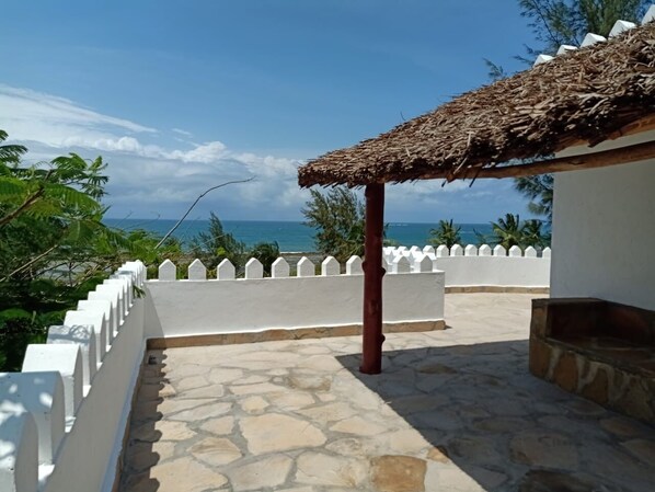 A stone-paved terrace with a white railing, a thatched roof structure, and a view of the ocean. - Villa with pool, stunning sea views, with own chef and staff on request (Msambweni)