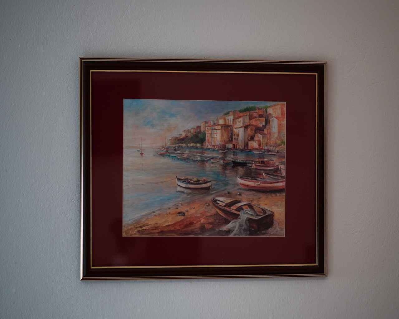 A framed painting of a coastal scene with boats and buildings.
