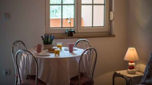 A dining area with a round table, four chairs, a window with a floral valance, and a table lamp. - Studio with internet access, near the sea (Vrbnik)
