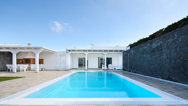 En swimmingpool med en mur av sten och vita möbler.