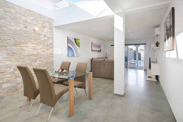 A modern dining area with a glass table and brown chairs, a stone wall, and artwork on the walls.