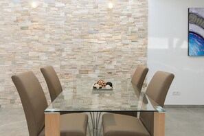 A conference room with a glass table, four chairs, a stone wall, and a painting.