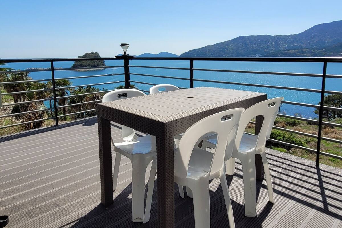 A terrace with a table and chairs overlooking a body of water and distant hills.