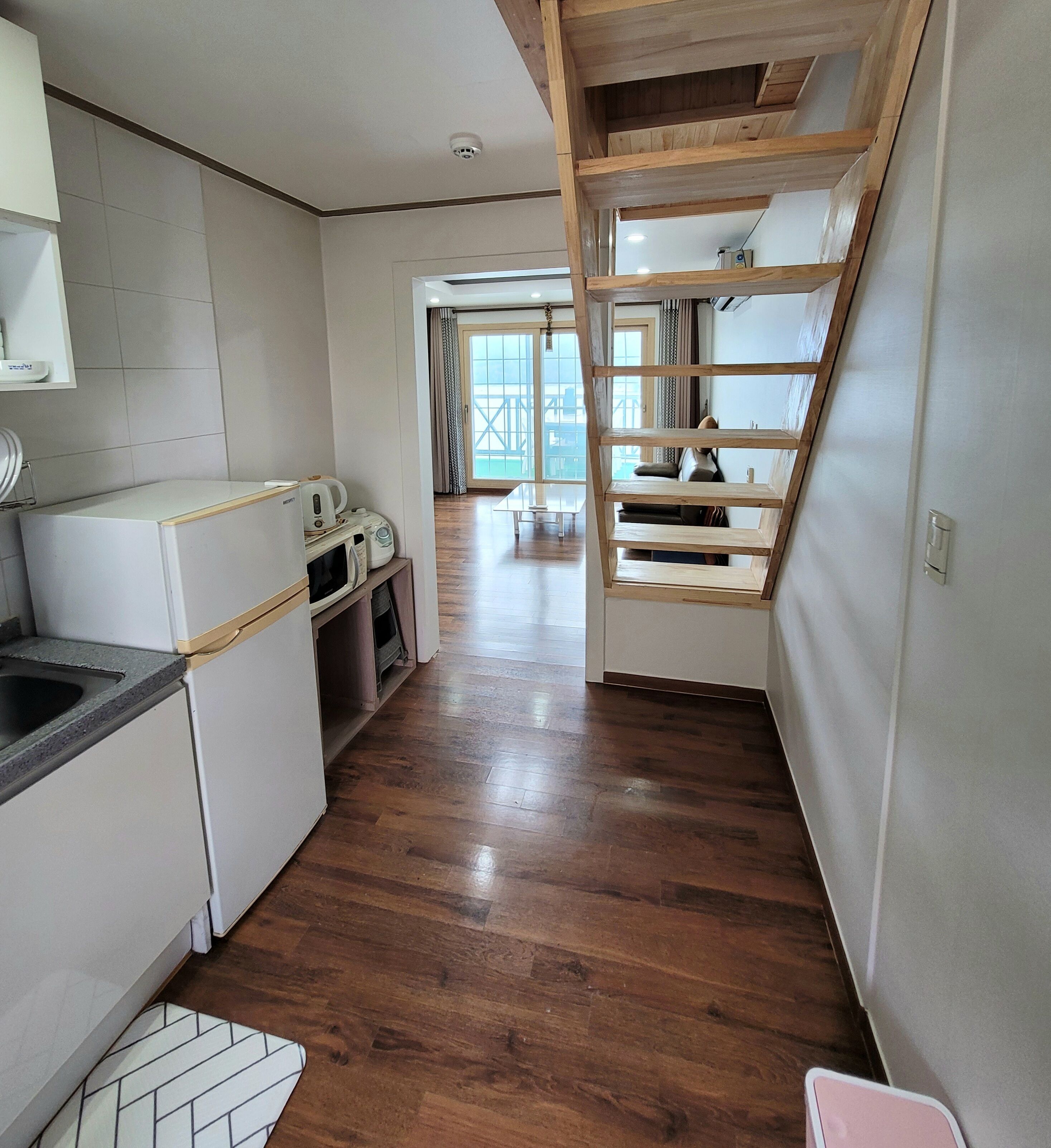 Una cocina estrecha con suelo de madera, horno empotrado y un lavamanos. Una escalera conduce a un balcón con vistas.