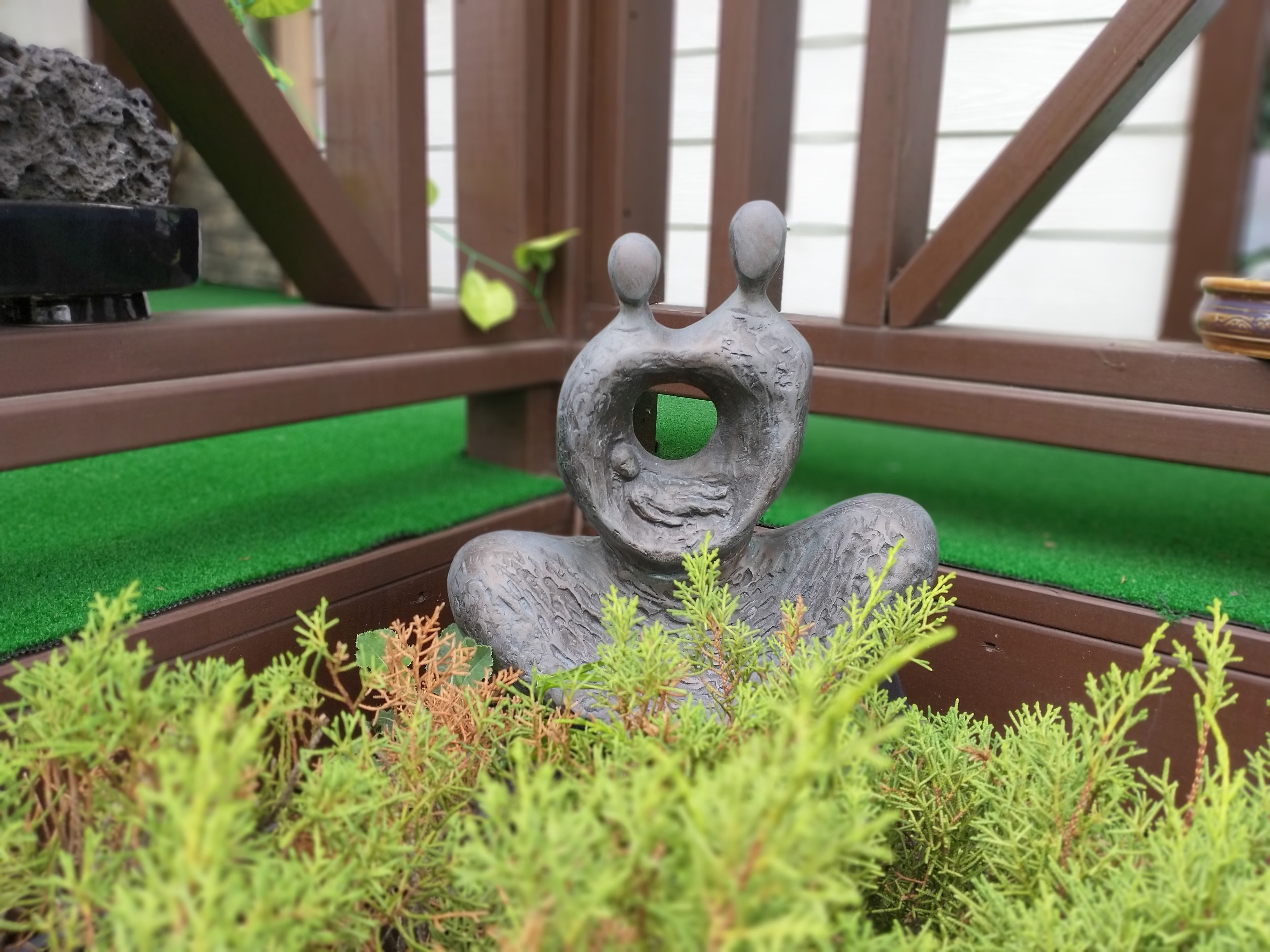 Escultura de una figura con un hueco en el centro, rodeada de plantas verdes.