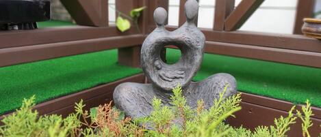 Escultura de una figura con un hueco en el centro, rodeada de plantas verdes.