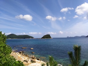 A coastal landscape with clear skies, rocky shoreline, and distant islands.
