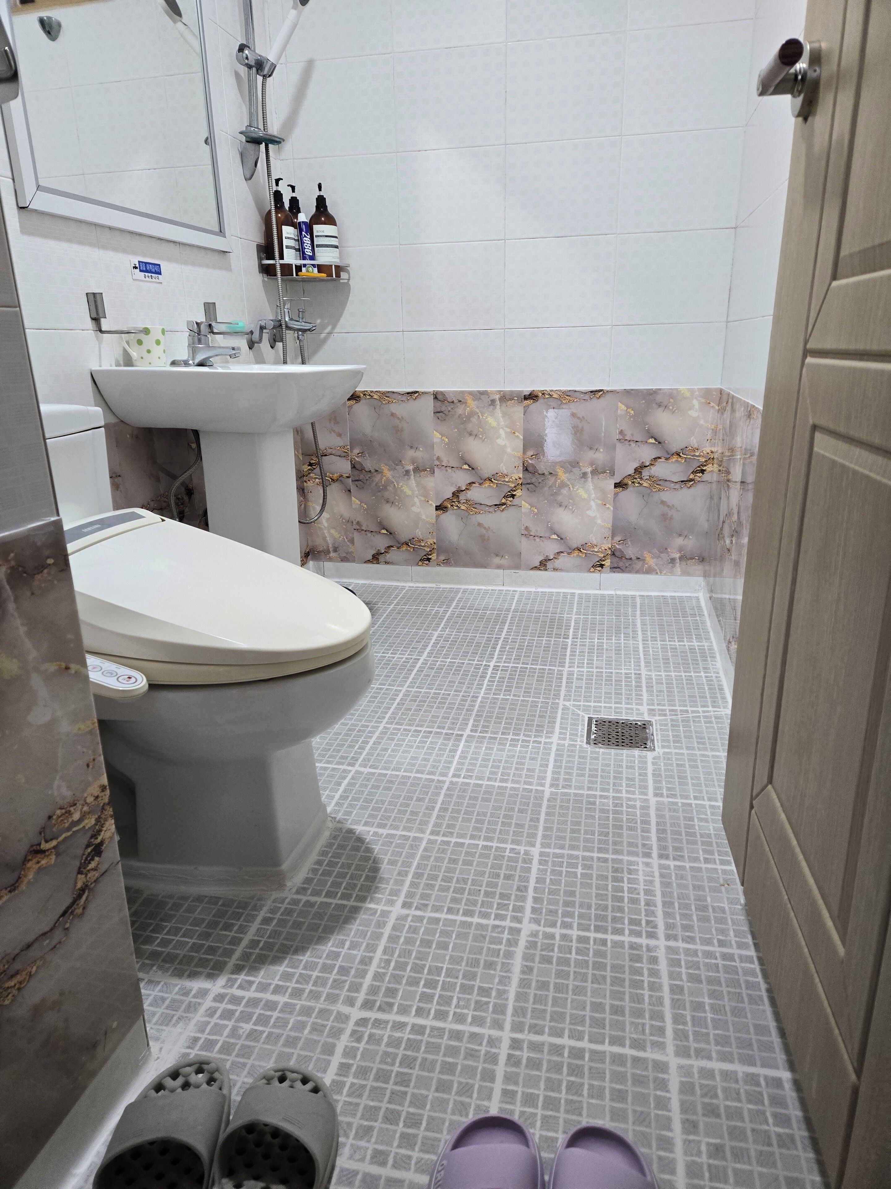 Un baño con inodoro, lavabo y ducha. Hay zapatillas en el suelo.