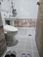 Un baño con inodoro, lavabo y ducha. Hay zapatillas en el suelo.