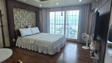 Una habitación de hotel con cama, televisor, ventilador, silla y balcón con vistas.