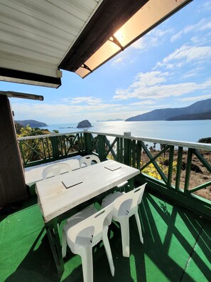 A covered outdoor seating area with a table and chairs, overlooking a body of water and distant landforms.