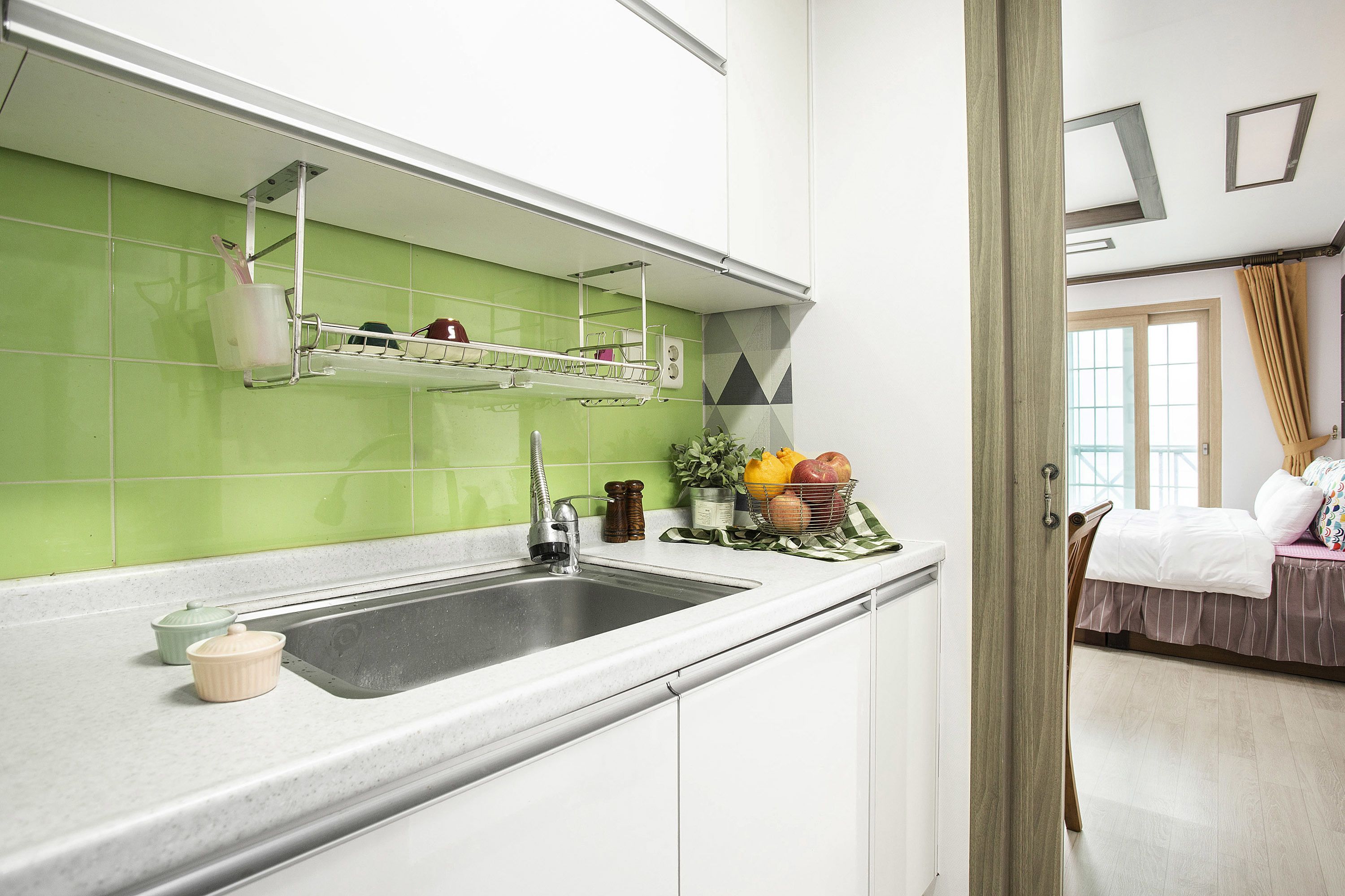 A kitchen with a stainless steel sink, a green backsplash, and a window with a view of the outside.
