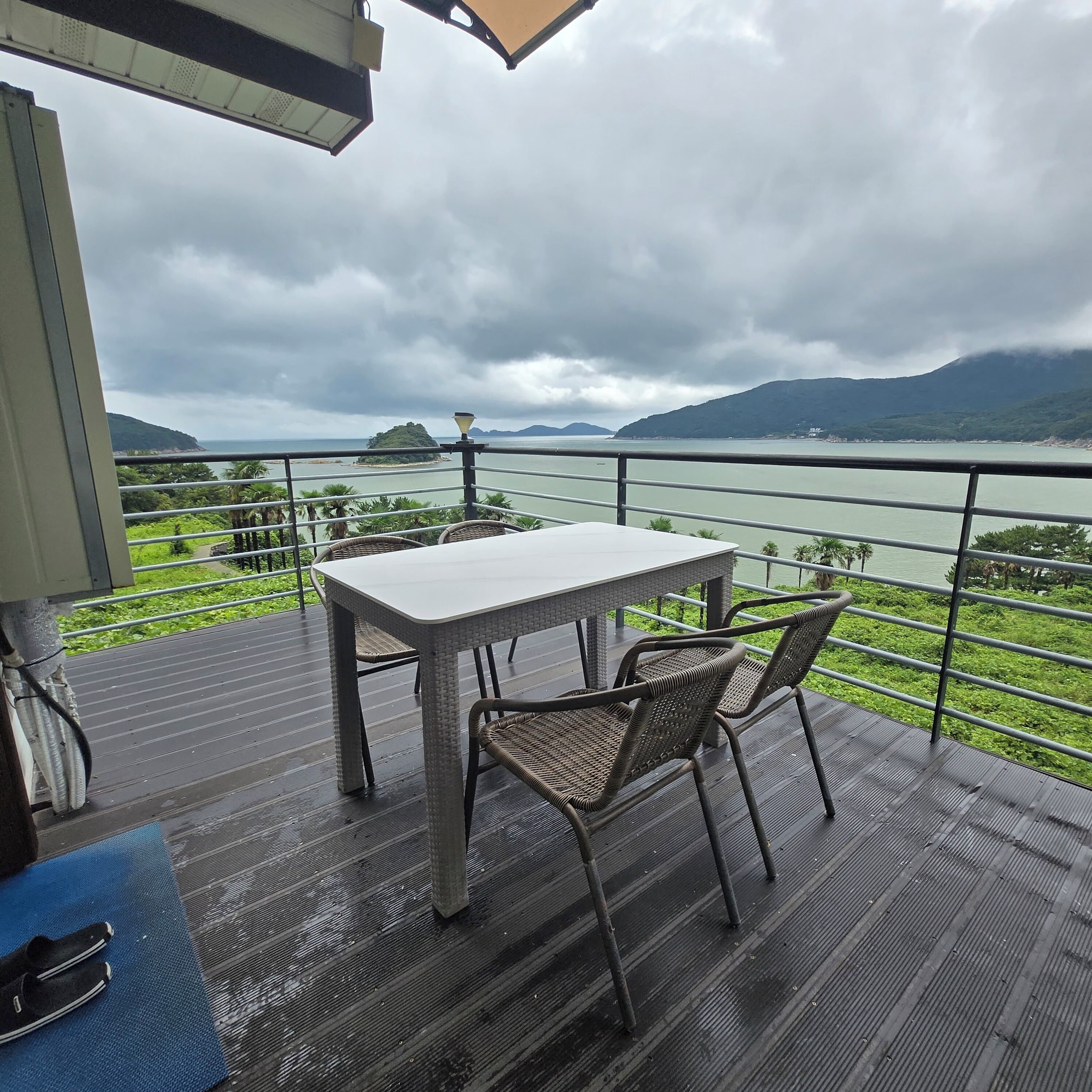 Un balcon avec une table et des chaises donnant sur un plan d’eau et des collines.