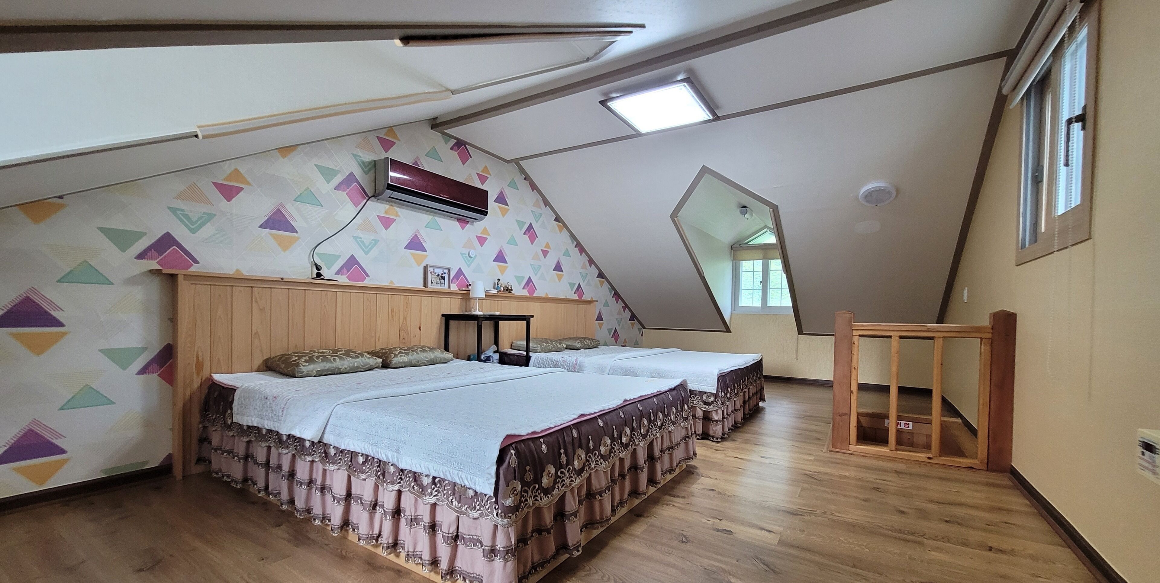 A bedroom with two beds, wooden flooring, a sloped ceiling, and a geometric-patterned wall.
