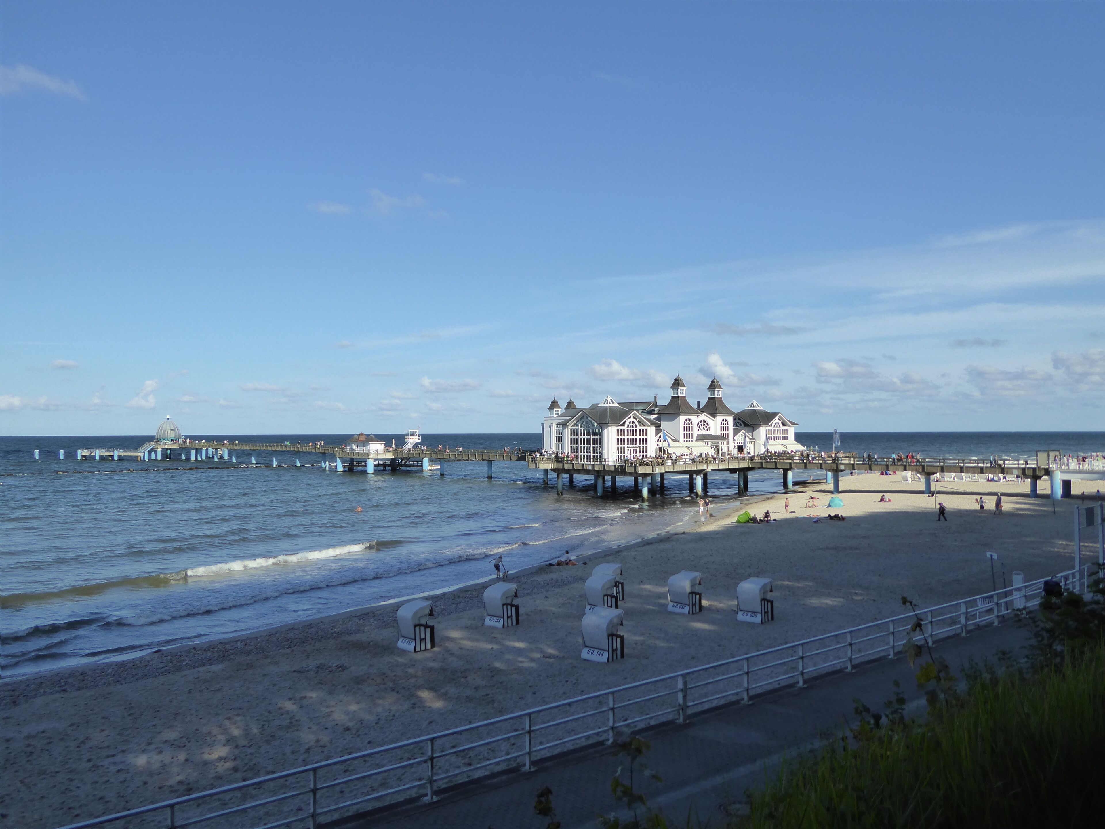 Un hôtel situé sur la côte, doté d’une jetée qui s’avance dans la mer, d’une plage de sable et d’un ciel dégagé.