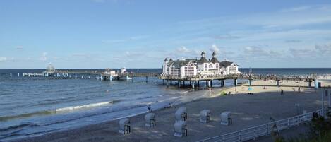 Un hotel frente al mar con un muelle que se adentra en el océano, una playa de arena y un cielo despejado.
