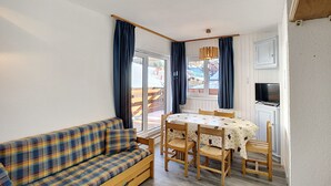 Een gezellige kamer met een geruite bank, een houten eettafel met stoelen en een televisie op een kast.