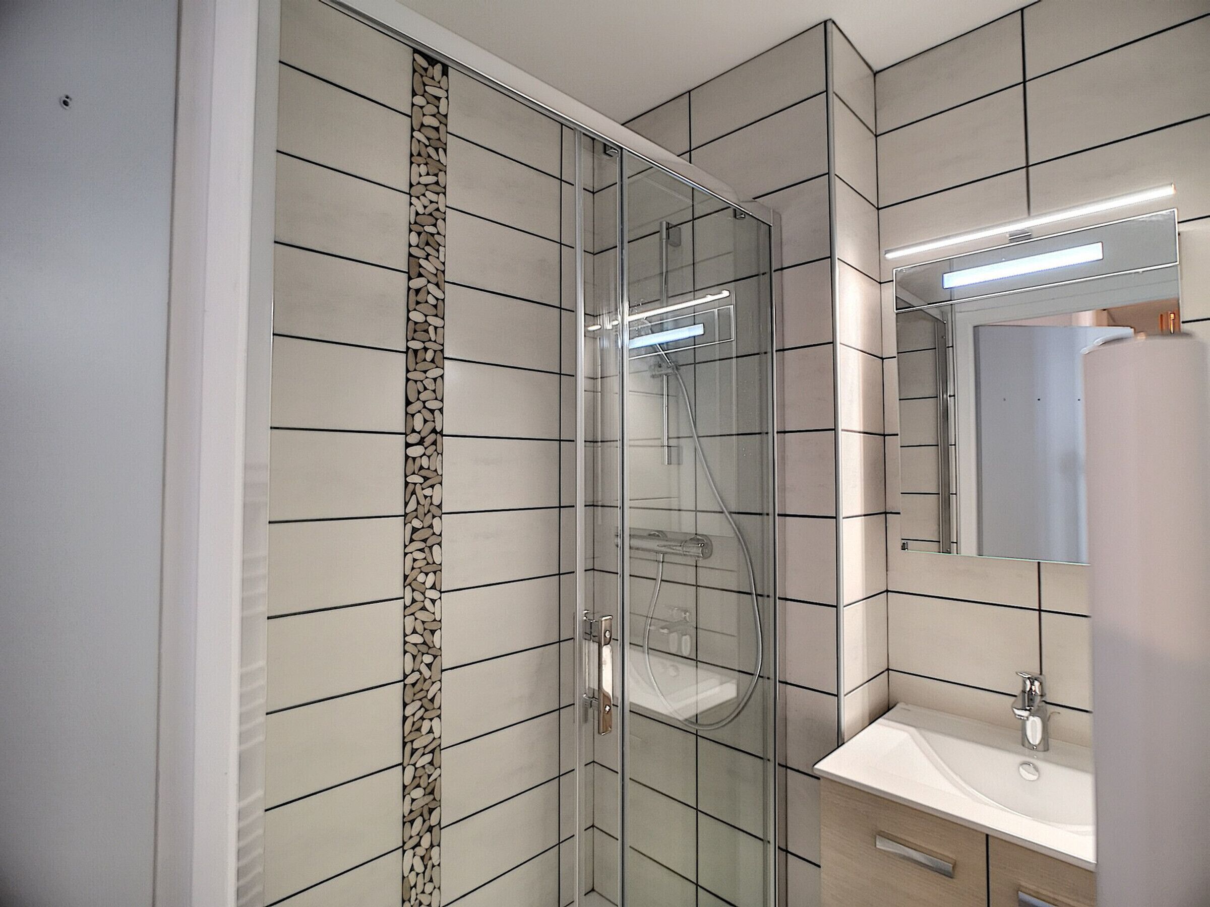 Un baño moderno con ducha de vidrio, lavamanos blanco y espejo sobre el lavamanos.