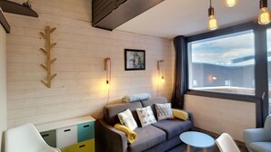 Un salon moderne avec un canapé gris, une petite table ronde et une chaise blanche. Deux lampes suspendues sont fixées au plafond.