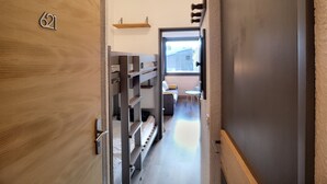 Un couloir étroit avec des lits superposés, une petite table et une fenêtre.