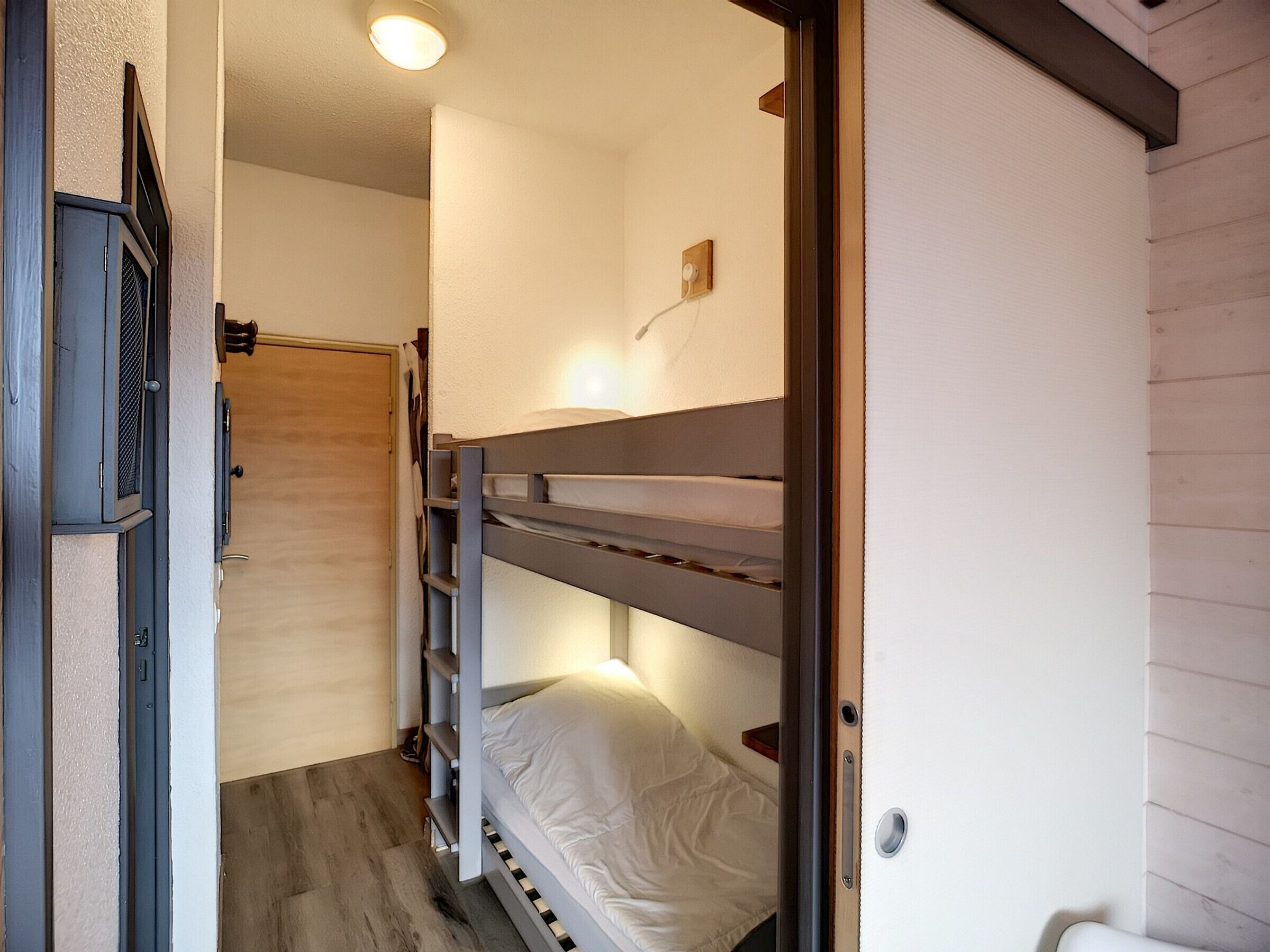 A bunk bed room with a door, a light fixture, and a small shelf.