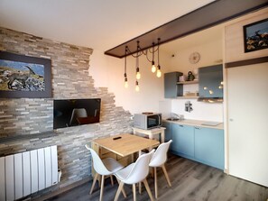 A modern kitchen with a stone wall, a dining area with a wooden table and white chairs, and a hanging light fixture.