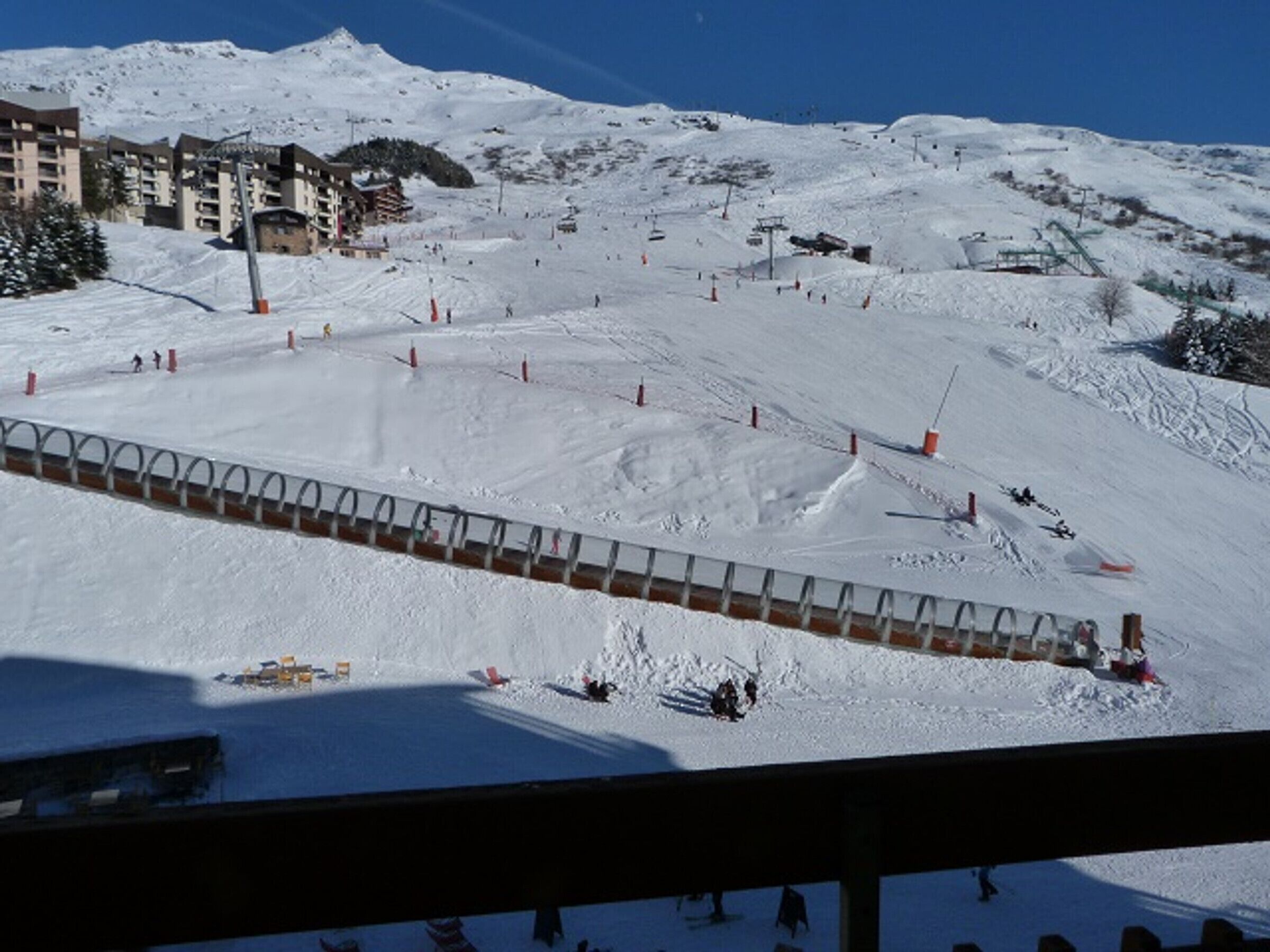 A snow-covered ski slope with a ski lift and buildings in the background.