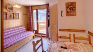 A cozy room with a wooden bench, a table with chairs, a painting on the wall, and a view through the door.