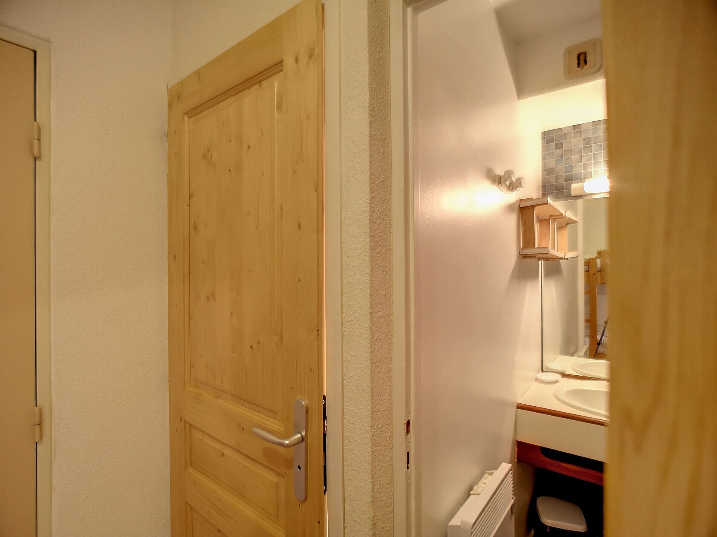 Eine Holztür mit silbernem Griff, eine weiße Wand und ein Badezimmer mit Spiegel, Waschbecken und Handtuchhalter.