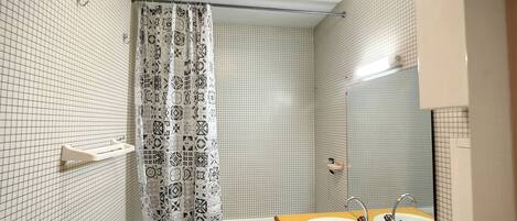 A bathroom with a white tiled wall, a patterned shower curtain, a white sink with a mirror, and a yellow vanity.