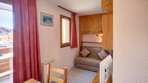 Ein gemütliches Zimmer mit einem Holzkabinett, einer gepolsterten Couch, einem Tisch und einem Fenster mit Vorhängen.