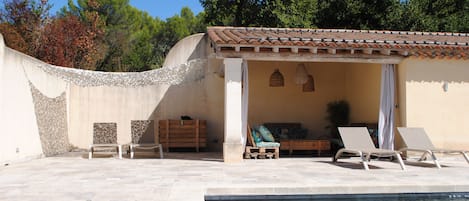 Área de piscina com espaço coberto para sentar, espreguiçadeiras e uma pequena mesa.