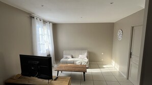 Et værelse med tv-stander i træ, en sofa, et træbord og flisegulv.