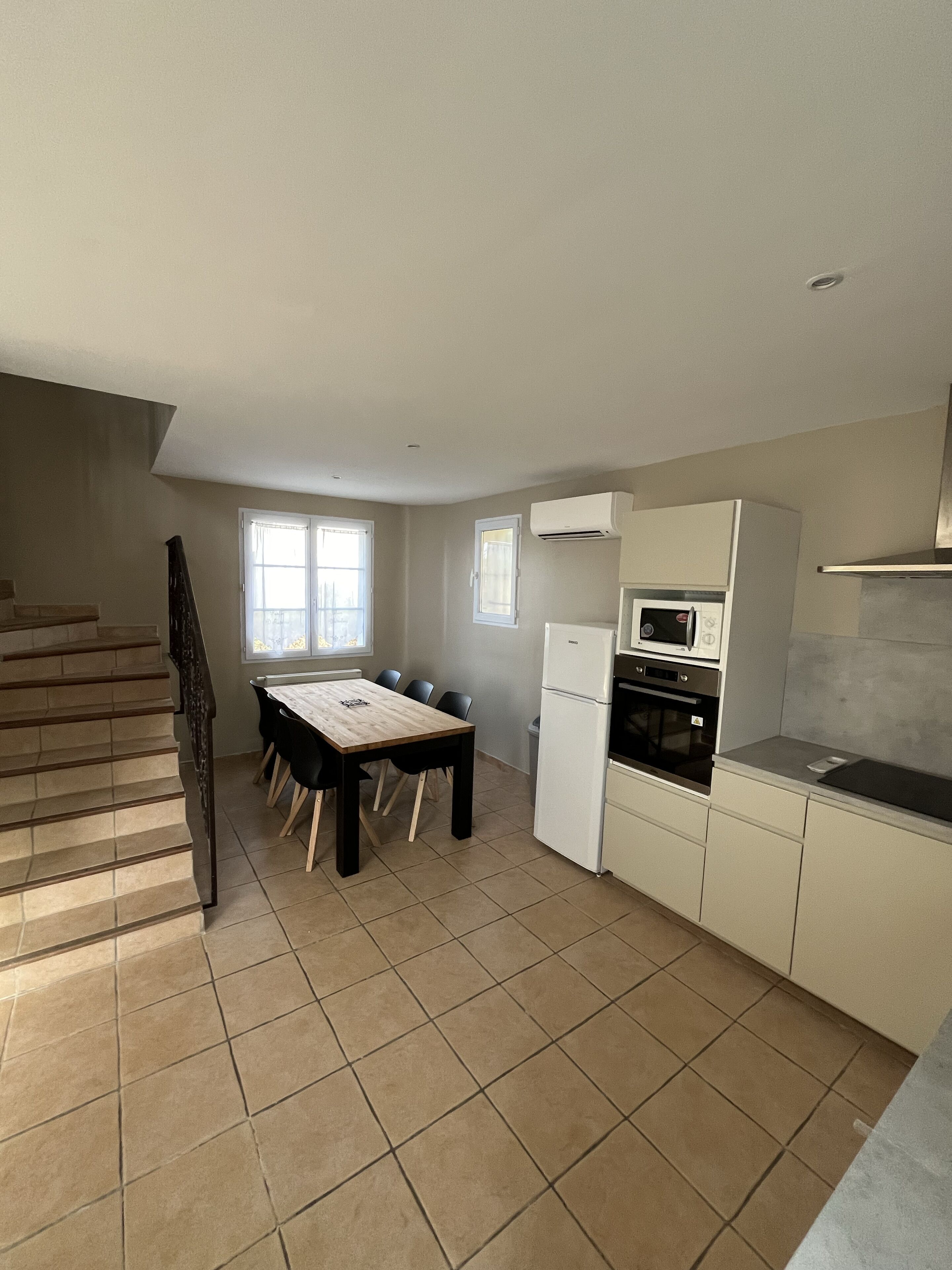 A kitchen with a dining table, chairs, a refrigerator, an oven, and a microwave.