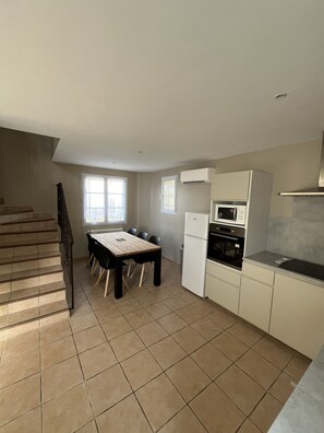 A kitchen with a dining table, chairs, a refrigerator, an oven, and a microwave.
