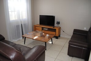 A living room with a wooden TV stand, a flat-screen TV, a lamp, a table with a tissue box, and two leather sofas.