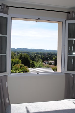 A room with a large window offering a view of a rural landscape with trees and buildings.