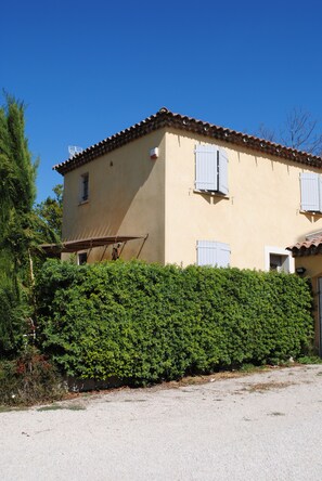 A two-story building with a beige facade, a tiled roof, and white shutters on the windows.