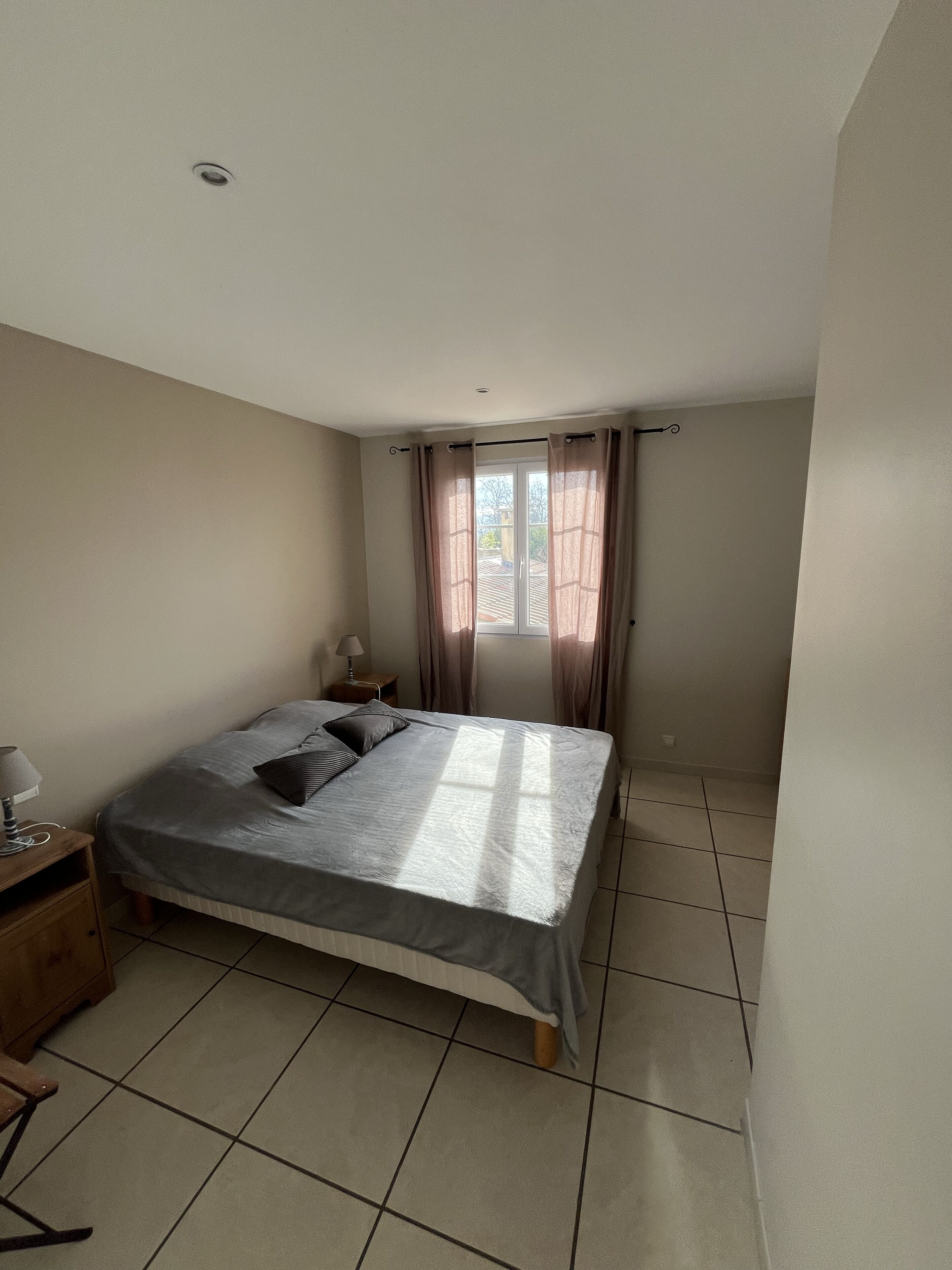 A bedroom with a bed, a nightstand, a lamp, and a window with curtains.