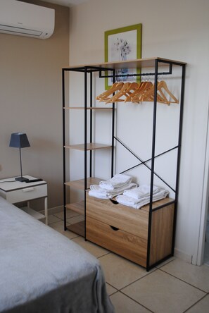 A room with a bed, a small table with a lamp, a wooden wardrobe with shelves, and a framed picture on the wall.
