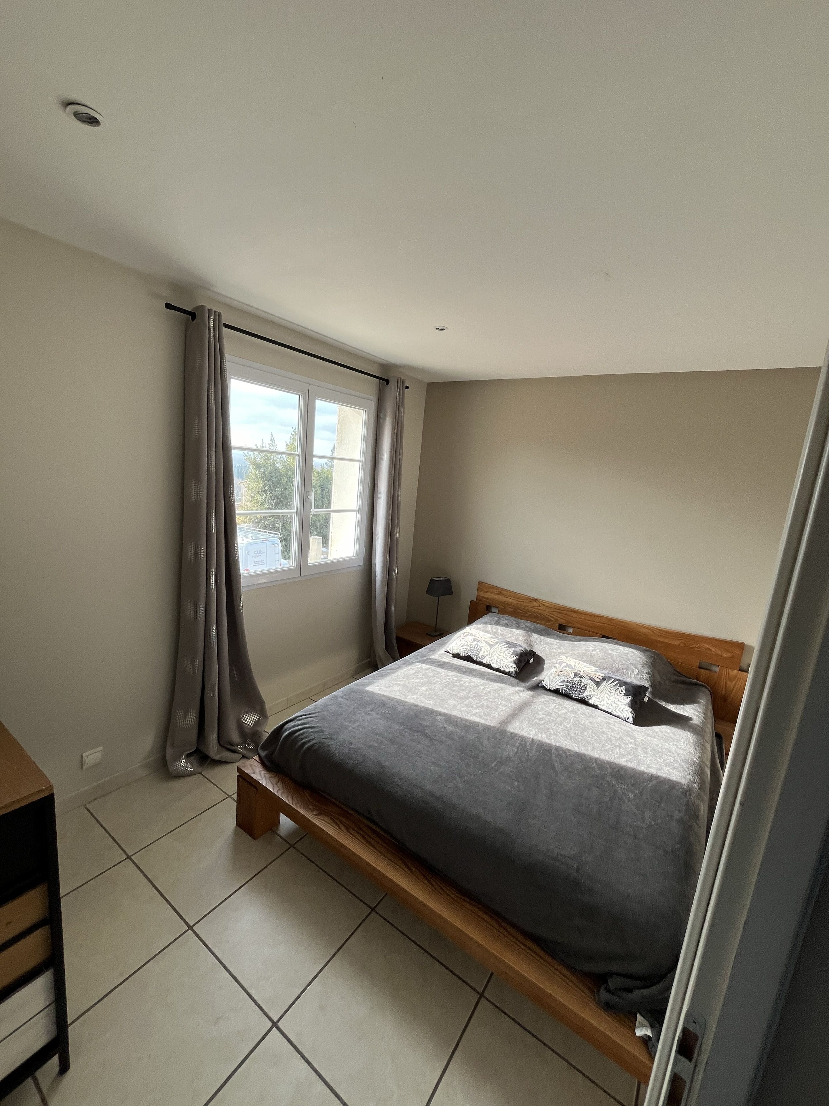 A bedroom with a bed, curtains, a window, and a nightstand.