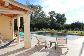 Un área junto a la piscina con una pérgola, sillas de descanso y una hamaca.
